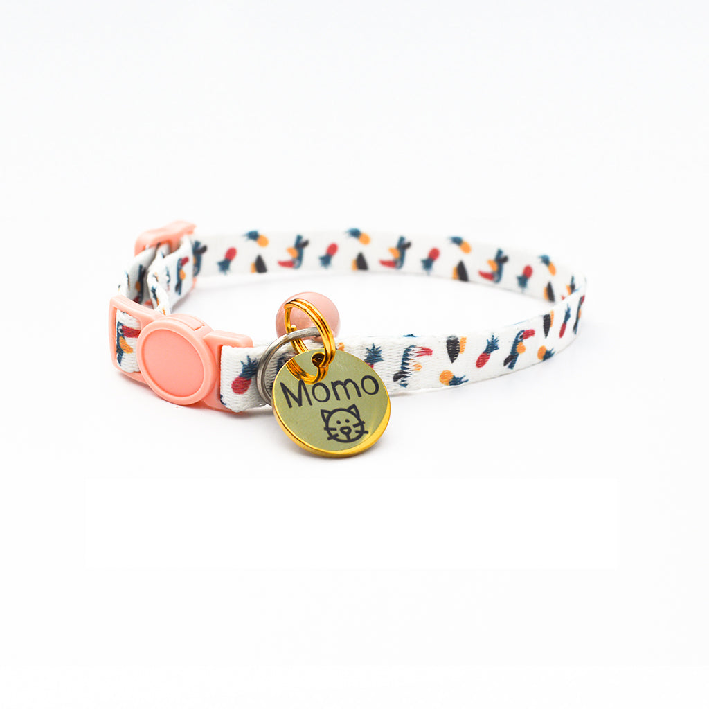 Colorful cat collar with a nature-inspired print, pink clasp, and a round gold ID tag engraved with the name "Momo" and a cute cat face icon.